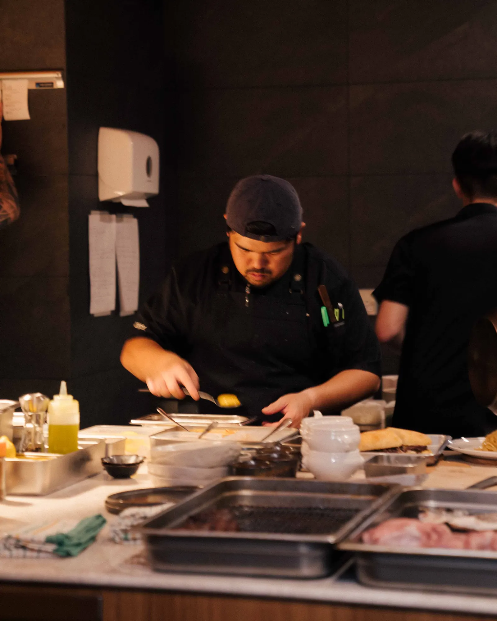 Chef in backwards cap plating with a spoon at the kitchen pass