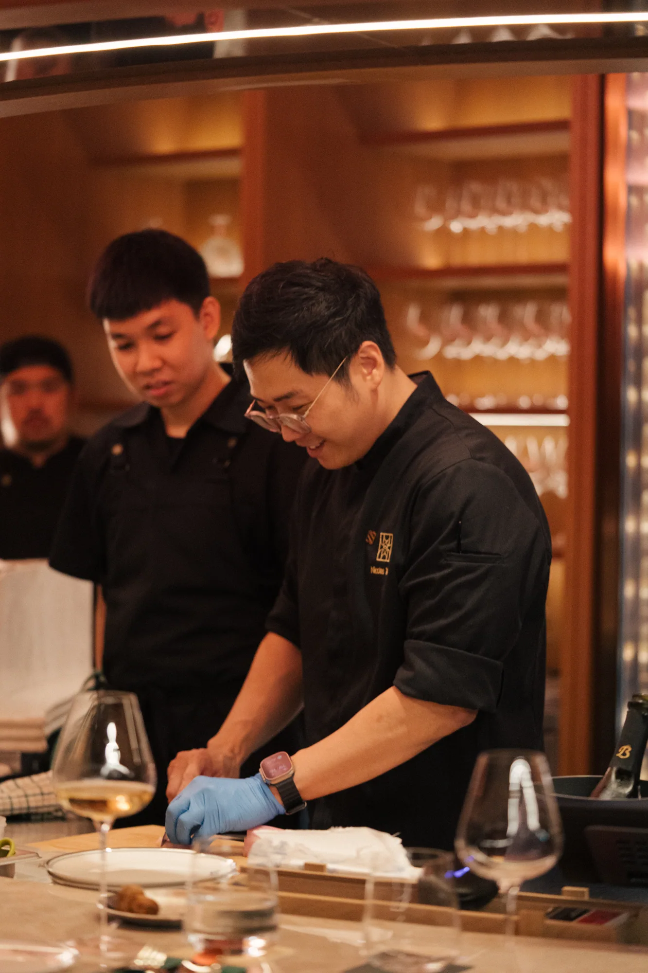 Gloved chef plating a dish at the pass