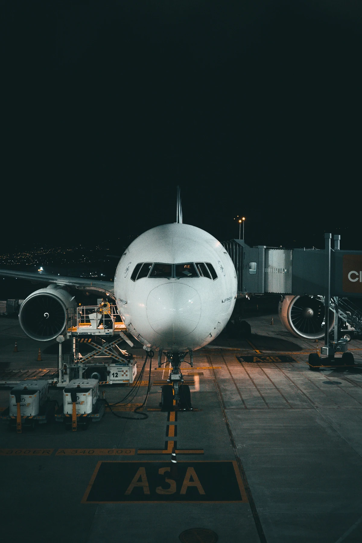 An airliner at the gate at night with ground crew servicing it