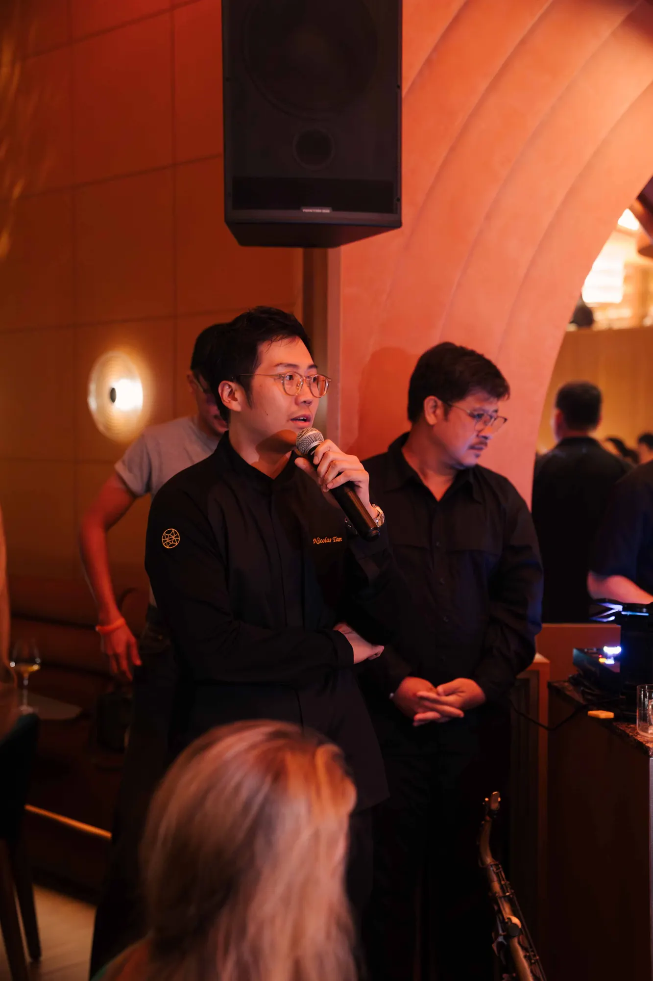 Man in a branded black shirt giving a speech with a microphone