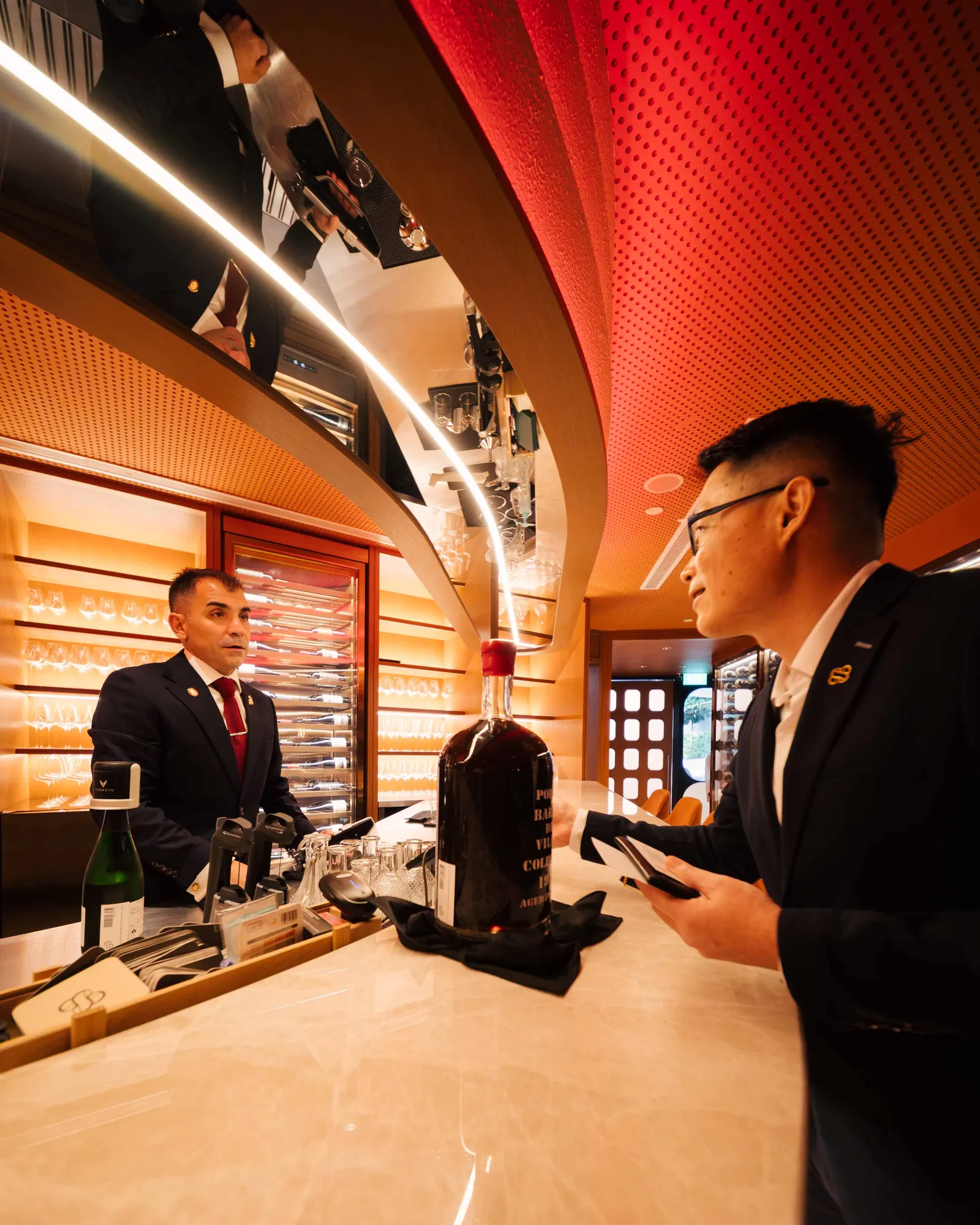 Sommelier behind the bar talking with a guest over a large bottle of wine