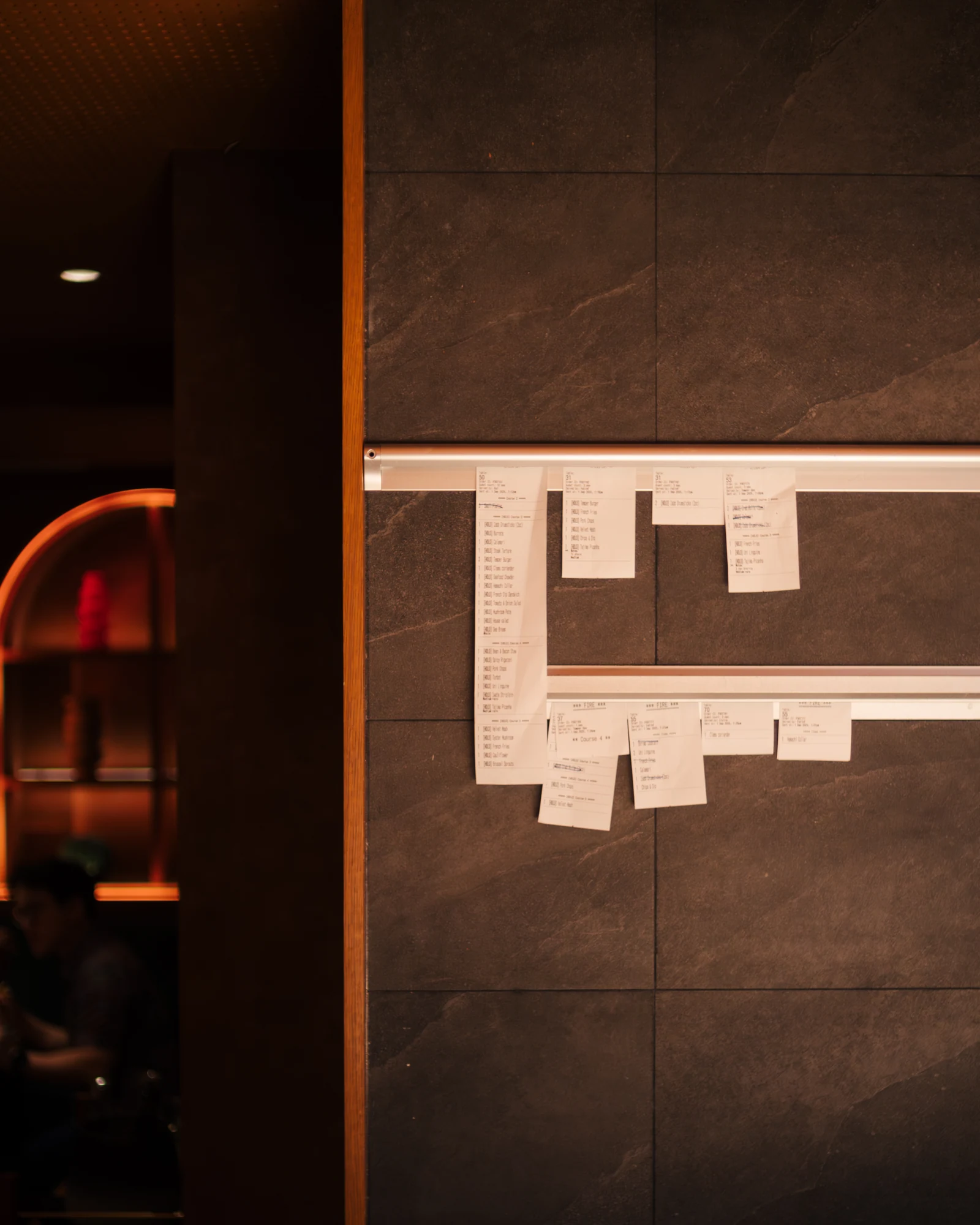 Order tickets clipped to a rail on a stone wall in a dim dining room