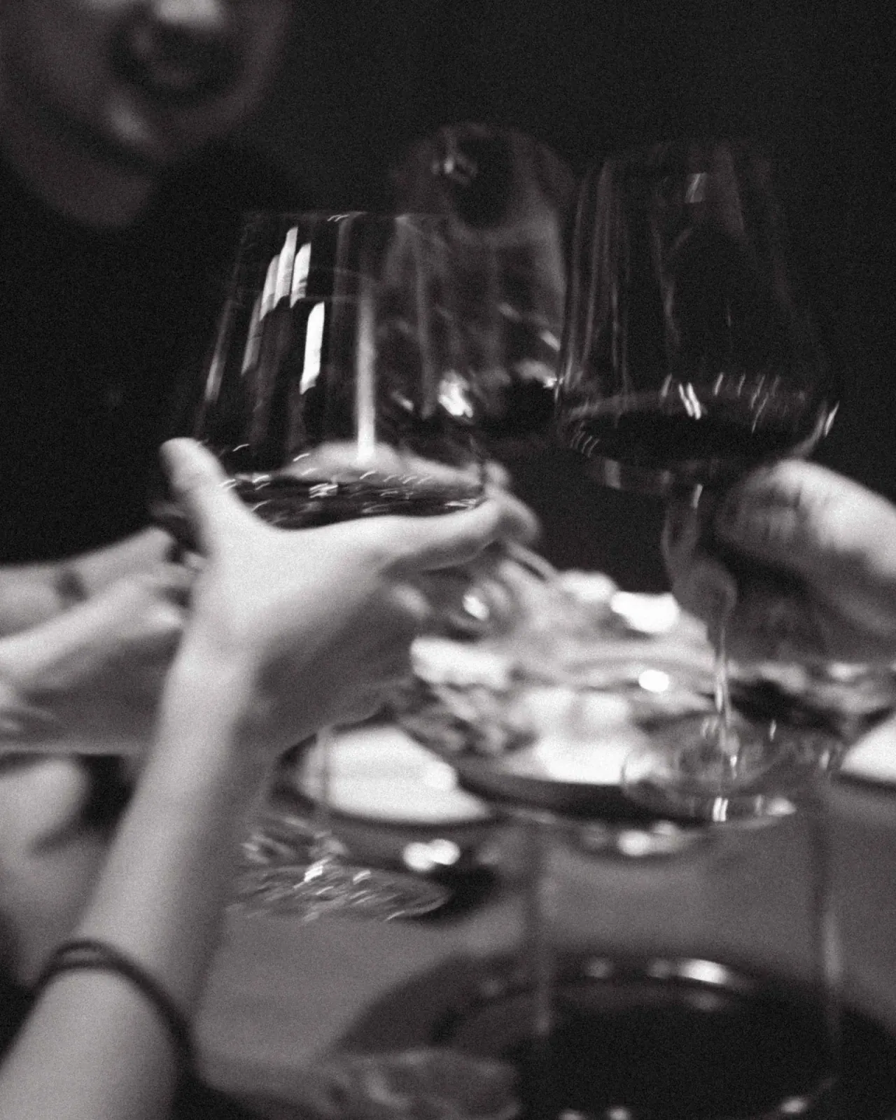 Black-and-white close-up of hands toasting with glasses of red wine